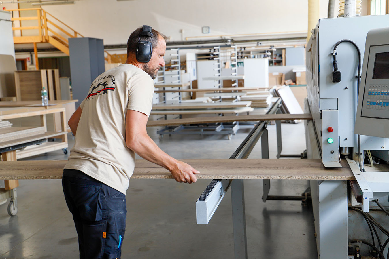 Un ouvrier de la Menuiserie Schreiber passe un panneau de bois dans une machine de finition. ©2023 Mathieu Improvisato