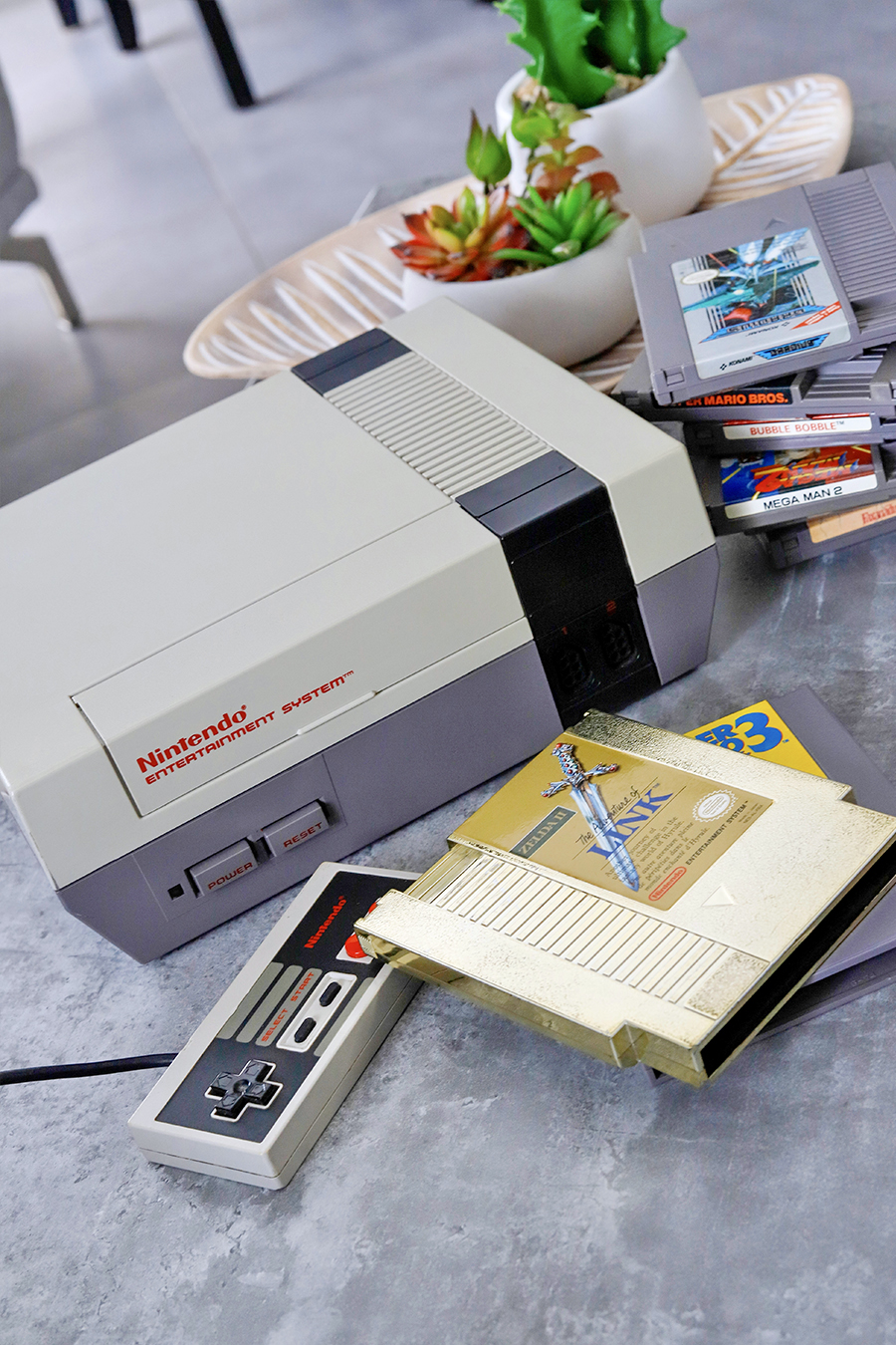 Console Nintendo NES avec une pile de jeu et une manette sur une table en pierre. ©2021 Mathieu Improvisato